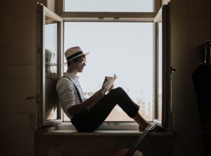 man sitting on window while reading